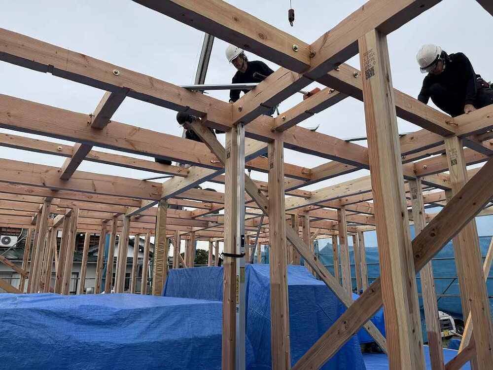 木造住宅の建て方工事で、職人が柱や梁に接合金物を取り付けている作業の画像。